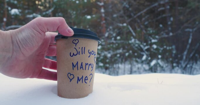 Will you marry me - yes, i will - Male and female hands put glasses with coffee in the snow with inscriptions.