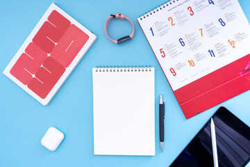 Vacation, trip or holiday planning concept - Public Holiday calendar with notepad, pen, earphone, sport watch and tablet on blue background. Top view flat lay copy space.
