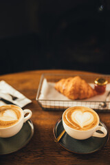 Two cups of hot cappuccino and croissants on wooden table.