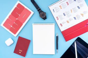 Vacation, trip or holiday planning concept - Public Holiday calendar with passport, notepad, pen, earphone, watch and tablet on blue background. Top view flat lay copy space.