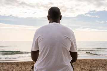 Low angle back view of unrecognizable African American male in casual white t shirt sitting on...