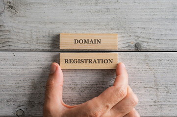 Male hand stacking two wooden blocks with a Domain registration sign on them