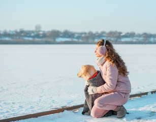 Young woman on winter ice river sitting with her dog golden retriever. Friendship, pet and human. woman playing with dog outdoors