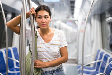 Overweary asian woman standing inside subway car and holding handrail.
