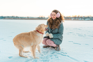 Big golden retriever dog giving a paw its owner on a background of winter ice river. Winter white landscape. Sunny weather. Friendship, pet and human.