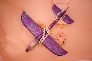 Lilac toy plane among pearl beads and flowers. Top view. Copy space