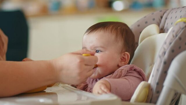 baby newborn eats. happy family dream weaning concept. dirty mess baby girl eating vegetables. baby daughter eats on a feeding indoors chair dirty face. naughty dirty babe indulges while feeding .