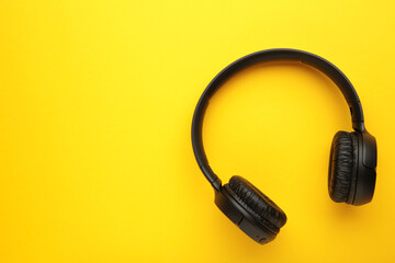 Black, modern wireless headphones on a yellow background.