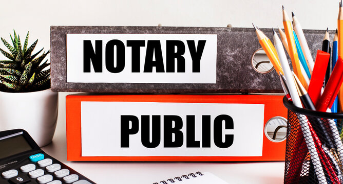 On the desktop there are two folders for papers with the text NOTARY PUBLIC, a calculator, pencils and a flower in a pot. Business concept