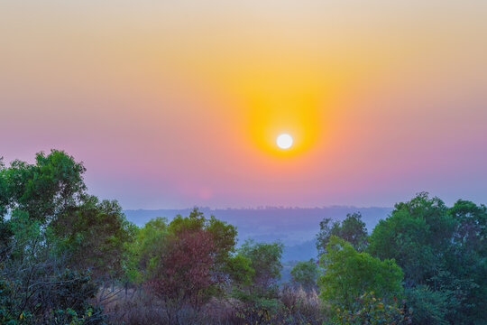 A sunset over a mountain. The sun's rays shining on the peaks create a range of colors, from warm oranges and yellows to cool purples and blues. 