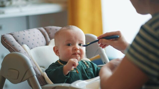 baby newborn eats. happy family dream weaning concept. dirty mess baby boy eating vegetables. baby son eats on a feeding chair dirty face. naughty dirty indoors babe indulges while feeding