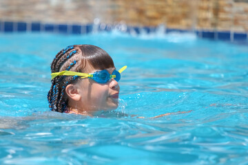 Young child girl in goggles exercises swimming in blue pool water. Summer recreation activity concept