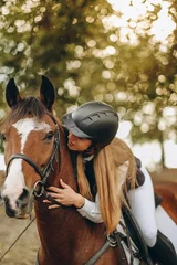Zelfklevend Fotobehang A young woman jockey lies on her horse and hugs her. © sergo321