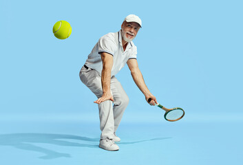 Happy look. Portrait of handsome senior man in stylish white outfit playing tennis over blue background. Concept of leisure activity, hobby, lifestyle