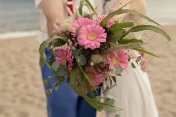 Brautpaar hält einen Brautstrauss mit pinken Gerbera auf einer Strandhochzeit