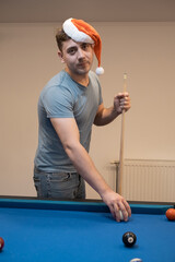 Fototapeta premium a man in a santa hat holds his hand on a pool table, plays snooker or prepares to shoot billiard balls, port game snooker billiards, billiard balls, play billiards