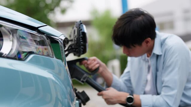 Asia man holding AC type 2 power cable plug connect to EV car at charging station. Car driven by electric motor engine for clean environment. Rechargeable vehicle concept. Ecology green technology