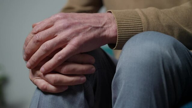 Close-up senior male hand rubbing ill knee indoors. Unrecognizable Caucasian man stroking leg sitting at home. Health care and aging concept