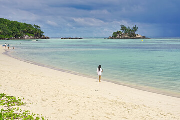 Young woman on the beach enjoying her holiday, looking at her phone of the picture taken, beautiful sunny day while arriving rainy clouds from the horizon