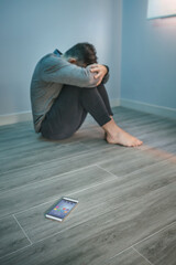 Unrecognizable man with problems sitting on the floor with mobile on the floor on foreground....