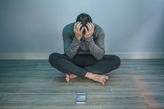 Unrecognizable man with problems covering face sitting on the floor behind of his mobile