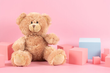 Baby kid toys background. Blue empty rectangle podium platform stand, teddy bear and pink wooden toy blocks on pastel pink background. Front view