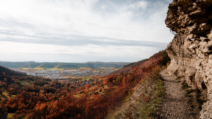 Wanderweg nah am Abgrund zum Tal bei Kalkfelsen und Aussicht auf eine Stadt im Herbst