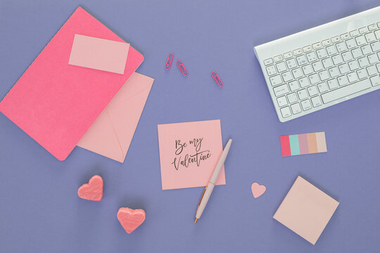 Overhead view of a computer keyboard, adhesive notes, heart-shaped candies and a note with the words Be My Valentine