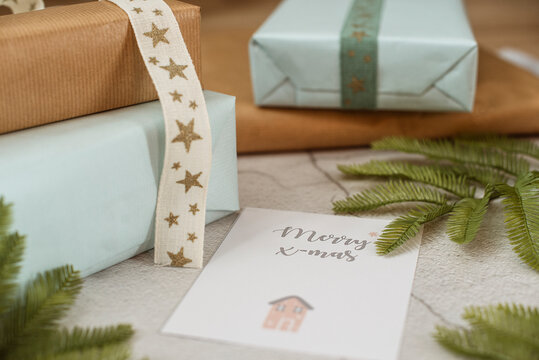 Close-up of wrapped rustic Christmas gifts, a Christmas card, ribbon and fir branches
