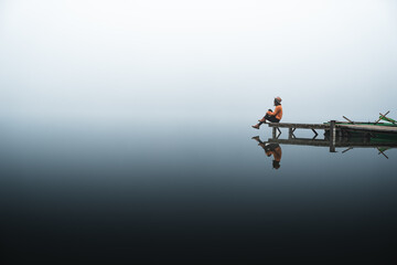 Side view of fashionable young woman standing on wooden dock looking at view on a misty morning....