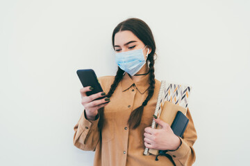 Young girl student in protective mask with phone and books