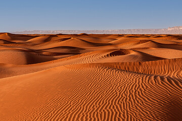 Rippled sand dunes in desert landscape with mountain backdrop, Saudi Arabia