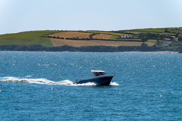 Fototapeta premium A small motor boat is sailing on the blue sea near the picturesque shores of Ireland. Seaside landscape on a sunny spring day.