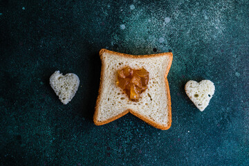 Overhead view of a slice of toast with heart shape cut out filled with jam