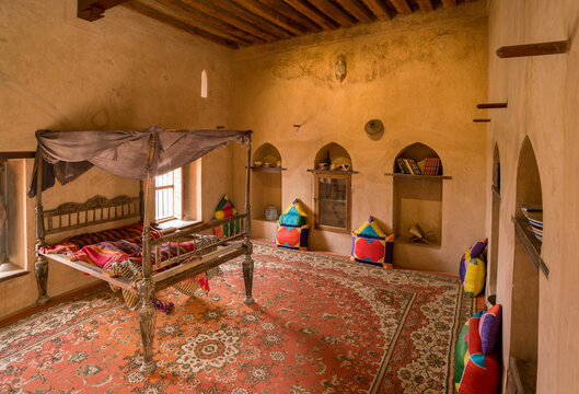 Nakhal, Oman - 04.03.2018: Room Of A Medieval Arabian Castle. Carpets And Pillow On The Floor, Holy Books On The Shelf. Fancy Bed. Fort Of Nakhal, Oman.