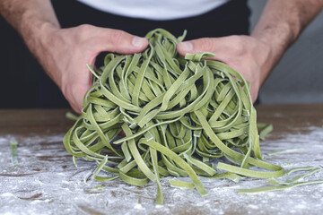 Fresh pasta. Homemade Italian raw pasta fettuccine with spinach in the hands of the chef on the background of the kitchen.
