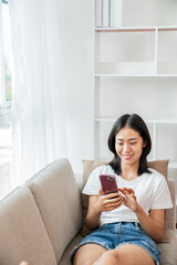 Asian Woman using cell phone sitting  on couch.