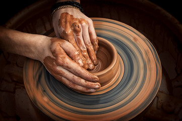 Potter's hands while working on the wheel, top view with dark background. Master makes a pot on a...