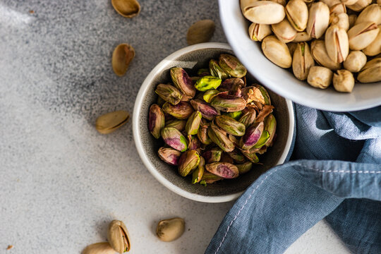 Overhead view of a bowl of pistachio nuts in shells next to a bowl of shelled pistachios