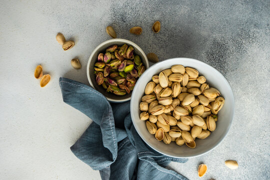 A bowl of pistachio nuts in shells next to a bowl of shelled pistachios