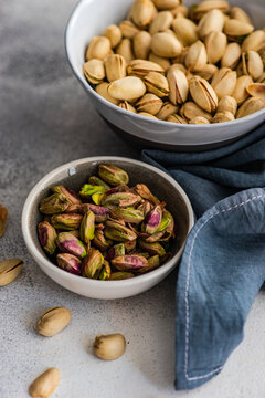 A bowl of pistachio nuts in shells next to a bowl of shelled pistachios