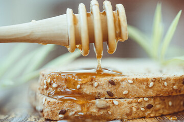 Close-up of a honey drizzler dripping honey on a slice of seeded brown toast