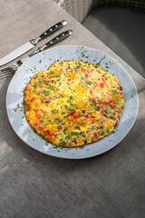 Filled omelette with tomatoes, red bell pepper and broccoli on light wooden table.