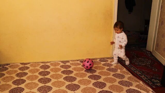Little baby is playing with a ball. Toddler boy who is beginning to learn to walk, loves football and is good at kicking it. Happy Kid. 
