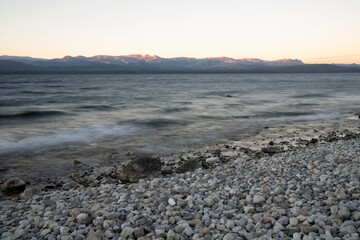 Long exposure shot of Nahuel Huapi lake at sunset. Beautiful blurred water effect, the rocky shore and dusk colors.