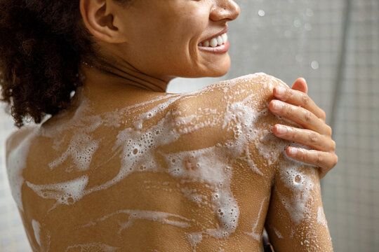 Close up of smiling african woman taking a shower with gel or shampoo foam in bathroom