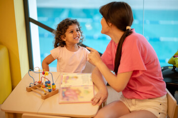 Young dark-haired woman playing with her kid in a play room