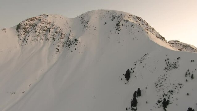 Drone approaches and flies towards a tall, snowy mountain peak in the Italian Alps after sunset - Corno Nero, Passo Oclini