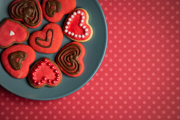 Top view of cookies in shape of hearts decorated by pink icing and bead sprinkles on gray plate on red background with dots