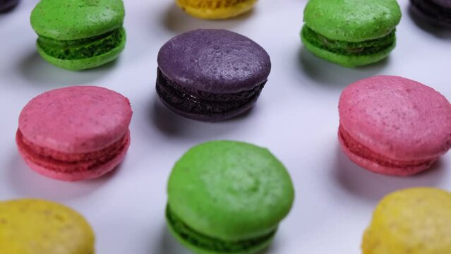 Rotating background of sweet macaroon cookies in different colors on a pink background